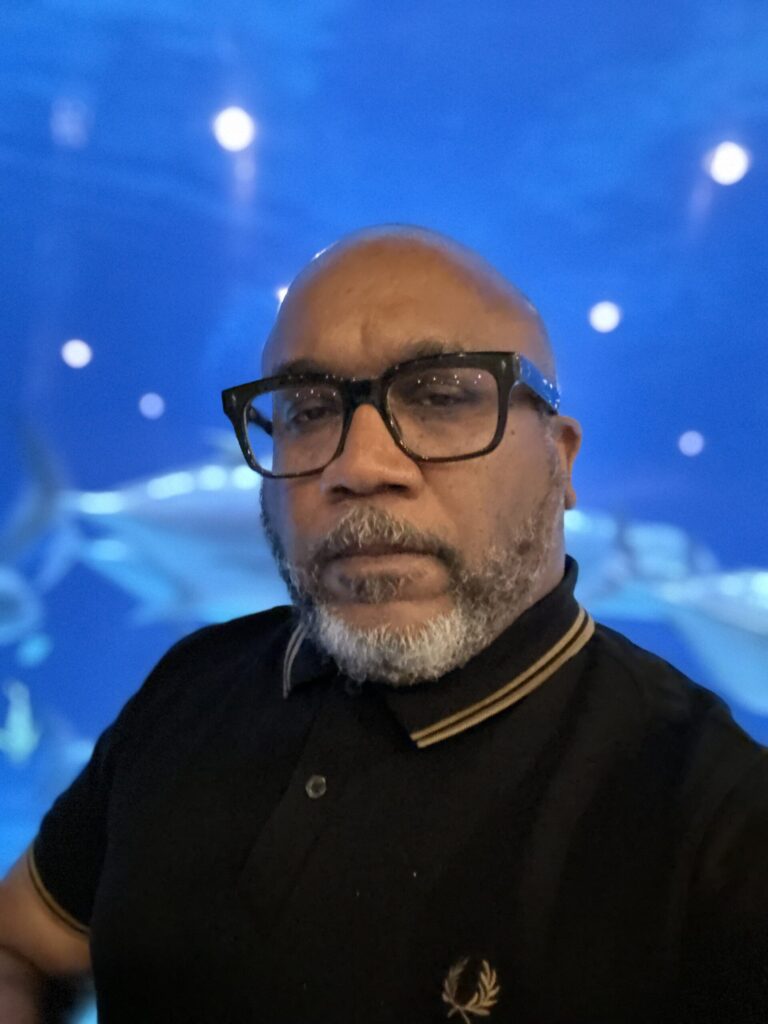 Photo of author. Wearing glasses. Black shirt. Gold accents.
